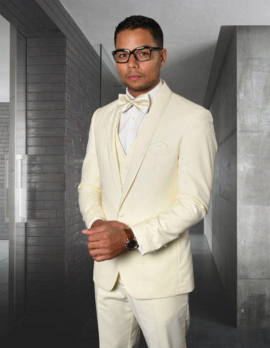 Dressed in the STATEMENT CLOTHING | CAESAR-OFFWHITE, a tailored fit ensemble by Statement Clothing featuring a bow tie and flat front pants, the person stands in a modern hallway with gray walls. With glasses perched on their nose, they exude sophistication and elegance in this chic ensemble.