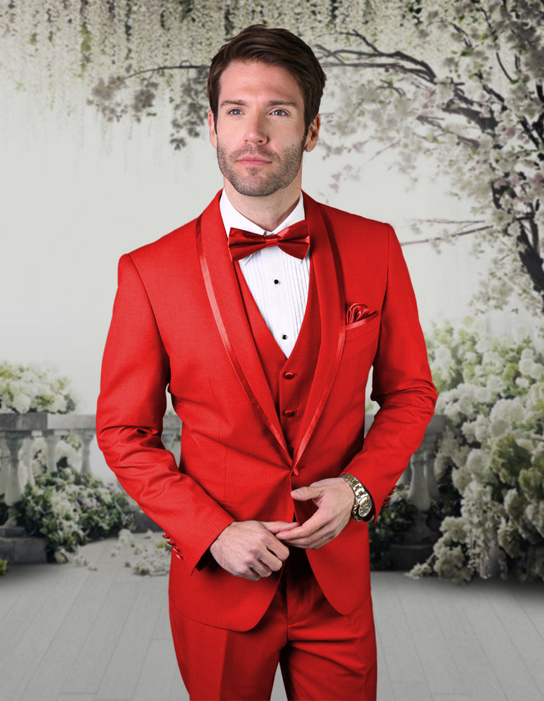 A person wearing the STATEMENT CLOTHING | CAESAR-RED tuxedo suit by Statement Clothing, crafted from fine Italian wool, stands against a floral and greenery backdrop, exuding elegance with its tailored fit and classic bow tie.