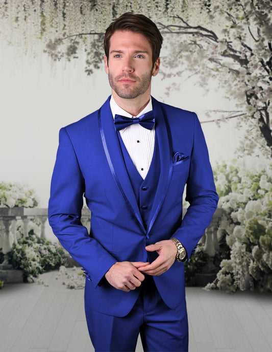 A man dressed in the STATEMENT CLOTHING | CAESAR-ROYAL tuxedo from Statement Clothing, featuring flat front pants and a bow tie, stands in a floral-themed setting, exuding elegance with its tailored fit.