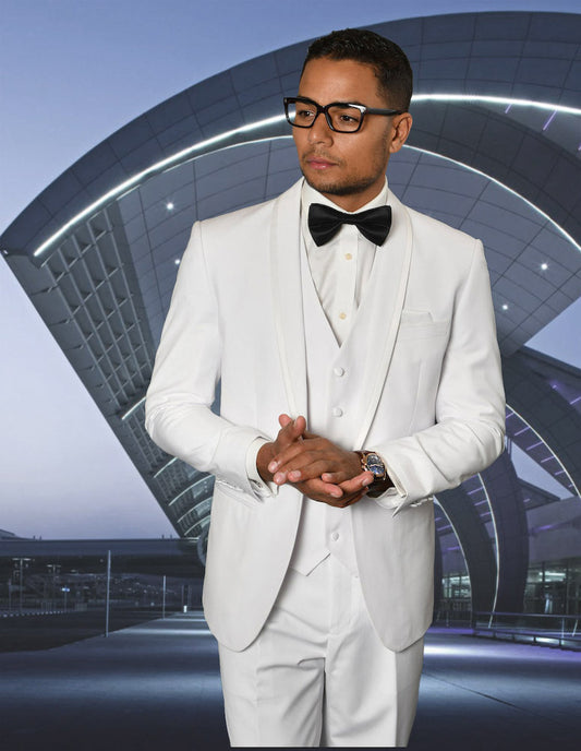 A man wearing the STATEMENT CLOTHING | CAESAR-WHITE tuxedo with a tailored fit and black bow tie stands in front of a modern architectural structure.