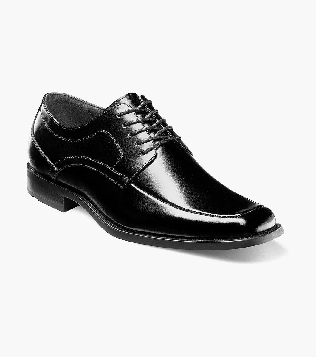 The Stacy Adams Calhoun Moc Toe Oxford, Model 20117-001, is a genuine leather dress shoe in polished black. This STACY ADAMS shoe features laces, a low heel, and boasts a sleek design. It is elegantly displayed against a white background.