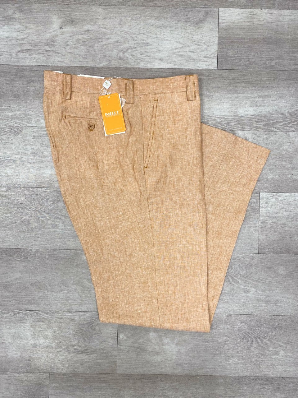 The Inserch Premium Linen Flat Front Pants P3116 in camel, featuring a classy casual style with a traditional silhouette, rest gently on the gray wood floor, still adorned with their original tag.