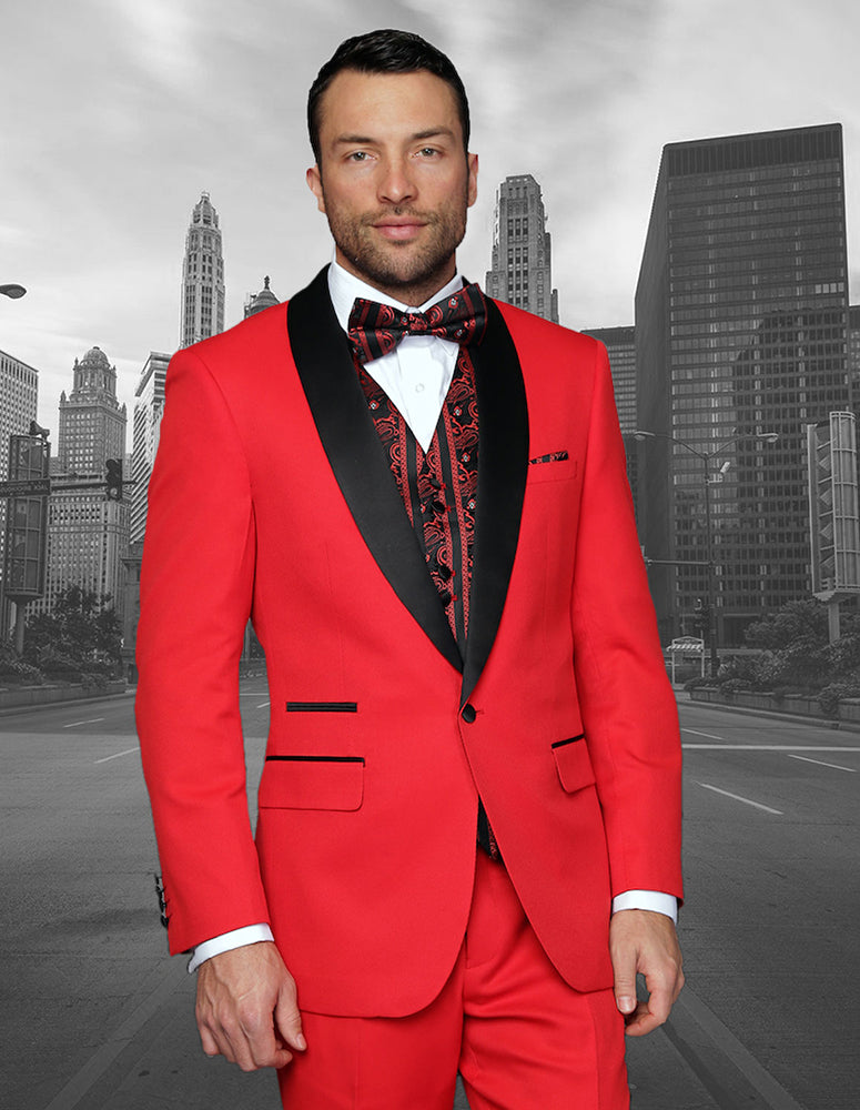 A man in a vibrant modern fit tuxedo from Statement Clothing's "CAPRI-RED" collection, featuring black lapels and a patterned bow tie, stands proudly against a grayscale cityscape background.