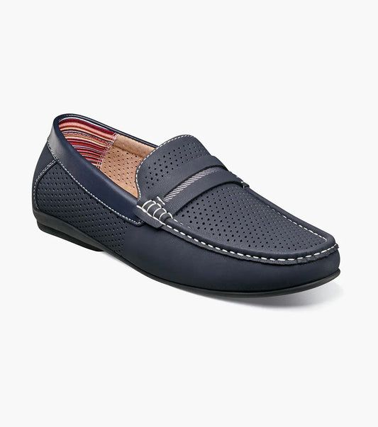 The Stacy Adams CORBY Moc Toe Saddle Slip On in Navy (Model 25513-410) features a perforated design, white stitching, and a strap across the top. It includes a leather footbed cover for enhanced comfort and showcases an interior with a striped pattern, making it an ideal casual shoe for warm weather.