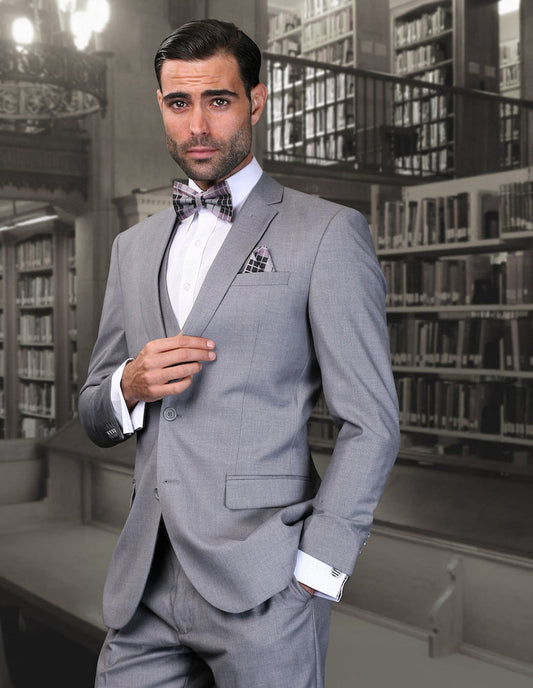 A man in a STATEMENT CLOTHING | CORTA-GRAY suit by Statement Clothing, tailored in an ultra slim fit with fine Italian wool, stands confidently in a library setting.