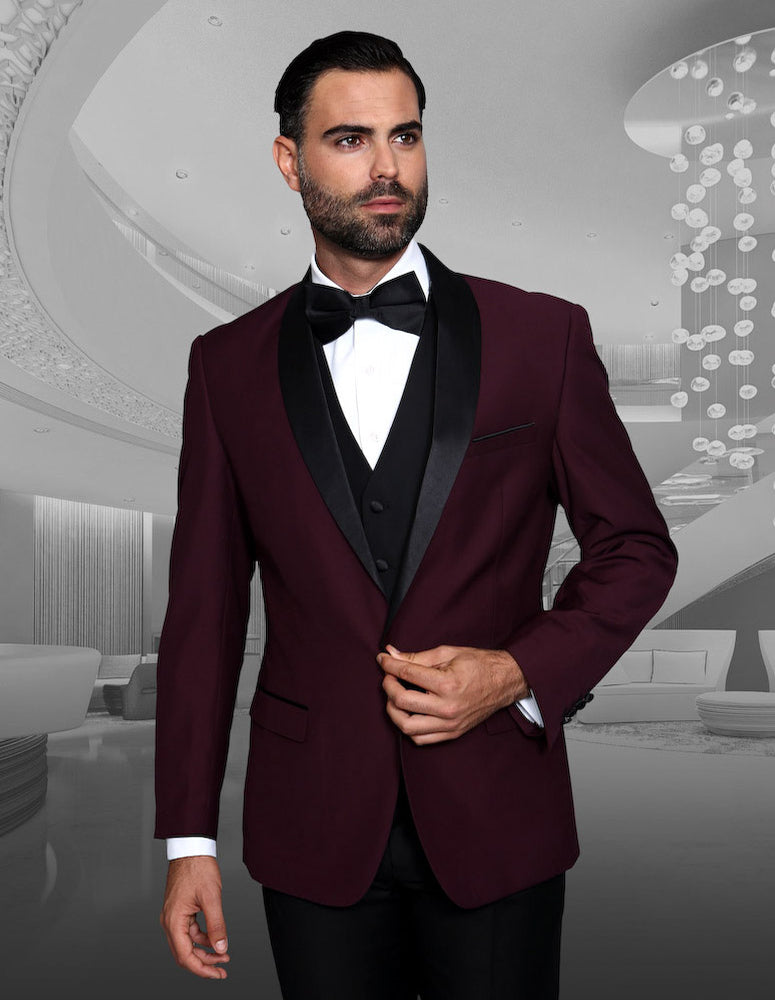 A man dressed in the STATEMENT CLOTHING | ENCORE-BURGUNDY dark, tailored-fit suit and burgundy bow tie from Statement Clothing stands confidently in an elegantly designed, modern interior.