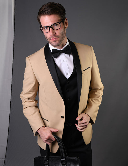 A man in glasses, wearing the Statement Clothing brand's ENCORE-CHAMPAGNE tuxedo jacket featuring a tailored fit and black lapel, paired with a white shirt and black bow tie, stands against a gray backdrop while holding a black briefcase.