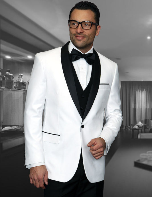 A man wearing the Encore-White tuxedo from Statement Clothing, featuring a tailored fit, stands in a modern room with a gray background. He complements his look with black glasses and a matching bow tie.