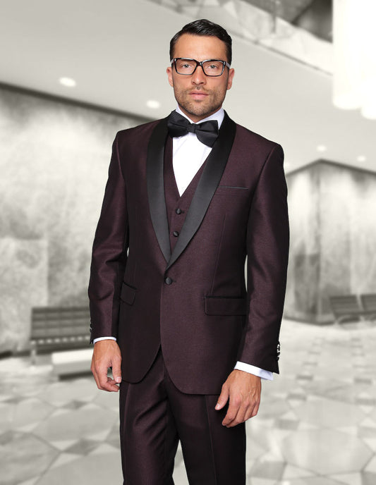 A man in a tailored fit, STATEMENT CLOTHING | ENZO-1-PLUM tuxedo and bow tie stands in a modern, spacious lobby.