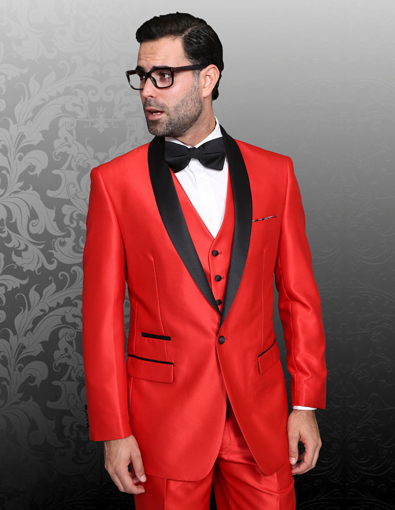 A man is dressed in a red tuxedo, specifically the STATEMENT CLOTHING | ENZO-7-RED by Statement Clothing, which features a tailored fit with a black shawl lapel and bow tie. He stands against a patterned grey background with dark hair and glasses.