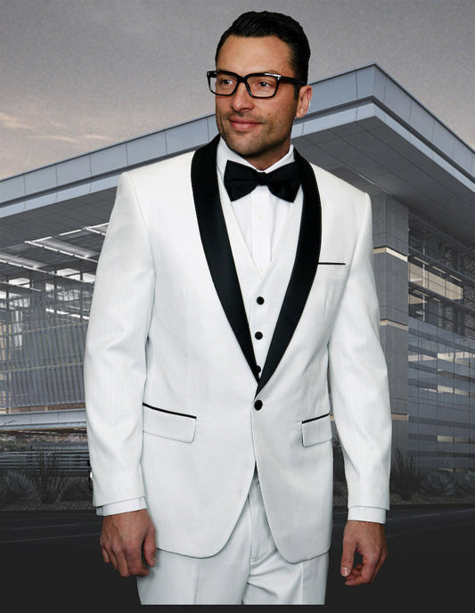 A man wearing the stylish ENZO-7-WHITE tuxedo by Statement Clothing, complete with a tailored fit and black bow tie, stands elegantly in front of a modern building.