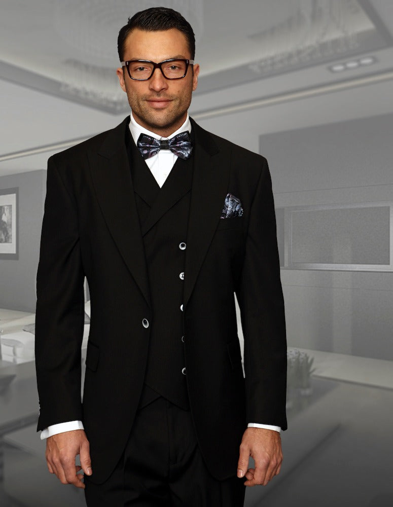 A man in a STATEMENT CLOTHING FLORENCE-BLACK tuxedo, along with a bow tie and glasses, stands in a modern, minimalist room.