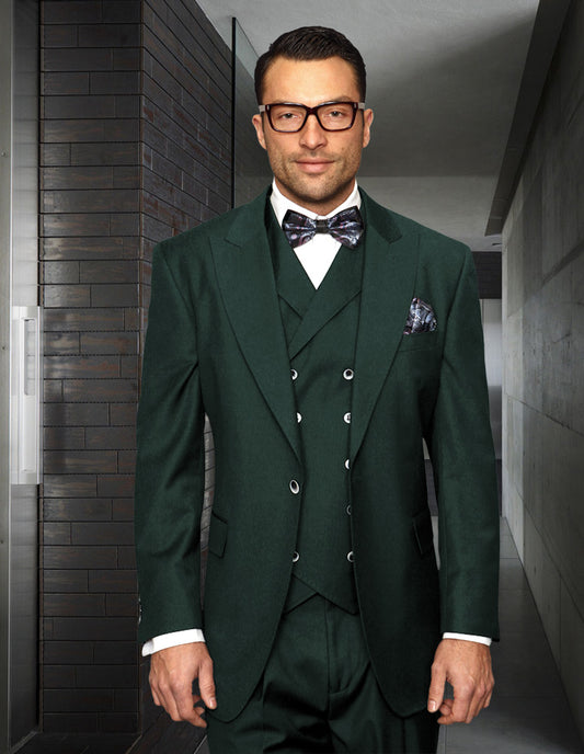 A man in a STATEMENT CLOTHING | FLORENCE-HUNTER by Statement Clothing, featuring an Italian wool three-piece suit in dark green and a bow tie, stands in a modern hallway, wearing glasses.