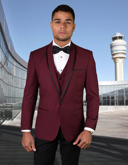 A gentleman wearing the STATEMENT CLOTHING | GENOVA-BURGUNDY tuxedo, tailored for a perfect fit, stands outside with the control tower looming in the background.