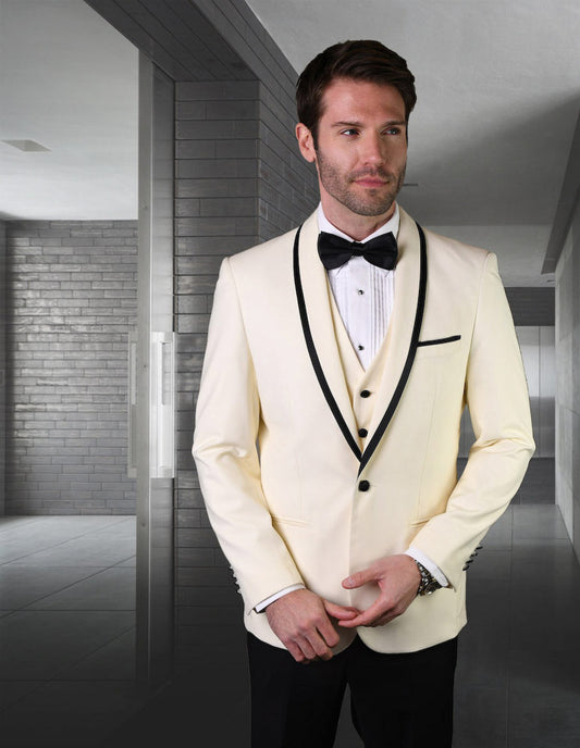 A man wearing the Statement Clothing GENOVA-OFFWHITE tuxedo, complete with a black bow tie and tailored fit, stands in a hallway with gray walls.