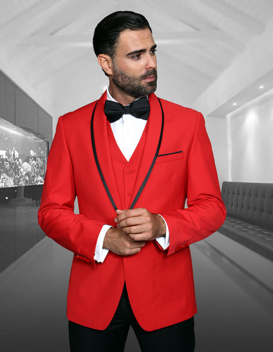 Sporting the GENOVA-RED from Statement Clothing, a man dons a tailored red tuxedo paired with a black bow tie as he stands in a room adorned with modern decor, including a fish tank and an elongated bench.