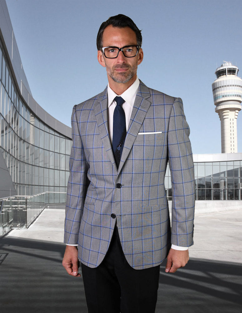 Dressed in a STATEMENT CLOTHING | GIGLIO-11-GREY suit by Statement Clothing, a man stands confidently in front of an airport terminal, the control tower majestically visible in the background.