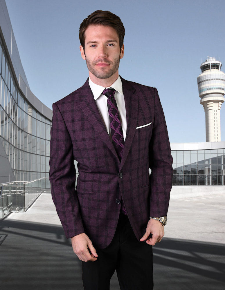 A man in a tailored fit, burgundy plaid suit stands outdoors, with a modern building and control tower in the background. The sleek design of his attire from Statement Clothing suggests it could be crafted from Super 150's fabric.