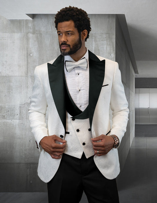 A man in the STATEMENT CLOTHING | HILTON-BLACK tuxedo suit, featuring a sophisticated white jacket with a black lapel from Statement Clothing, stands elegantly in a sleek room with concrete walls.