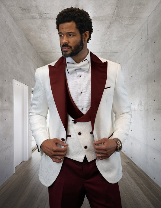 A man wearing the Hilton-Burgundy tuxedo from Statement Clothing stands in a concrete hallway, adjusting his bow tie.