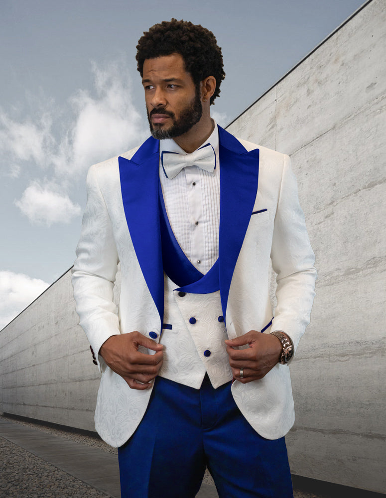 A man wearing the HILTON-ROYAL tuxedo by Statement Clothing, featuring a white and blue design with a bow tie, stands in front of a modern concrete wall, exuding royal style with its elegant modern fit.