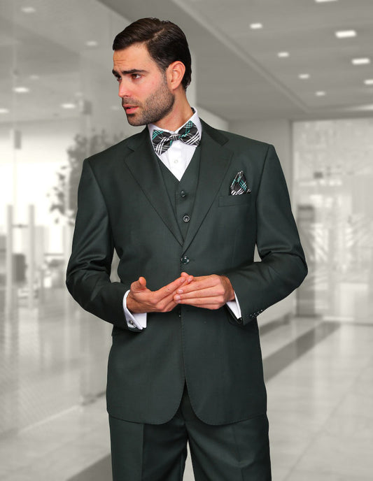 A man in a tailored fit dark suit, specifically the STATEMENT CLOTHING | STZV-100-HUNTER by Statement Clothing, along with a bow tie, stands in an office corridor, gesturing with his hands.