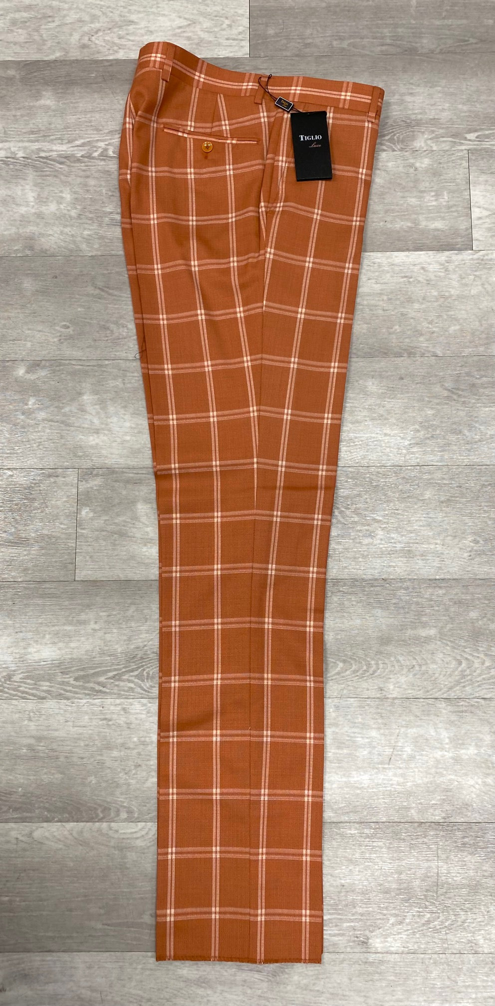 The Tiglio Luxe 2560 rust plaid flat front trousers, a Modern Fit piece from Tiglio Luxe, showcase a buttoned back pocket and have a black tag attached. Made from pure extrafine wool, these sophisticated trousers are presented on a wooden floor.