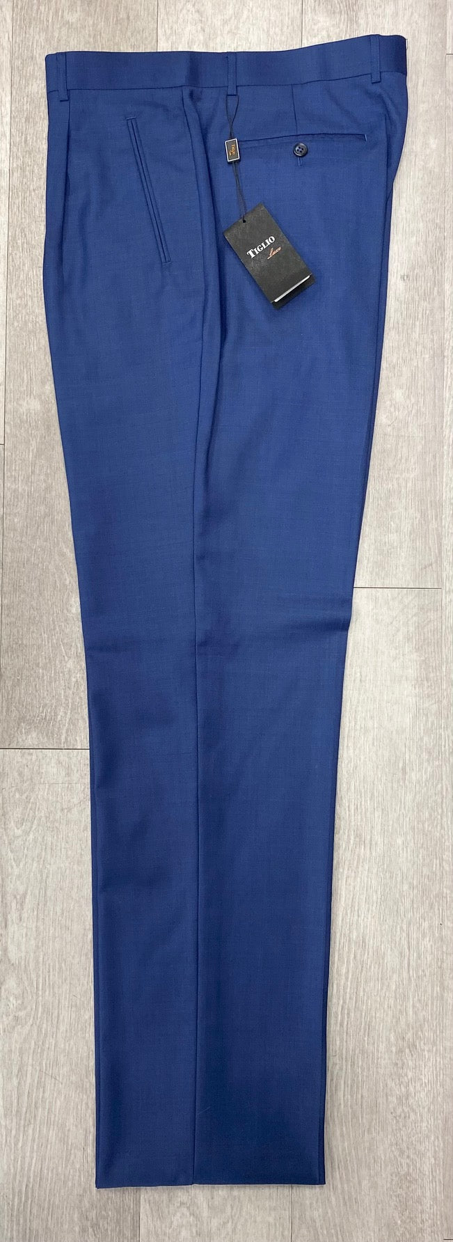 Tiglio Luxe 2521 Comfort Fit Single Pleated Pants, featuring an 18+ inch leg and available in size 48 only, are displayed on a wooden floor. These blue pants, with a pocket and fitted with a tag, highlight their relaxed fit perfectly.