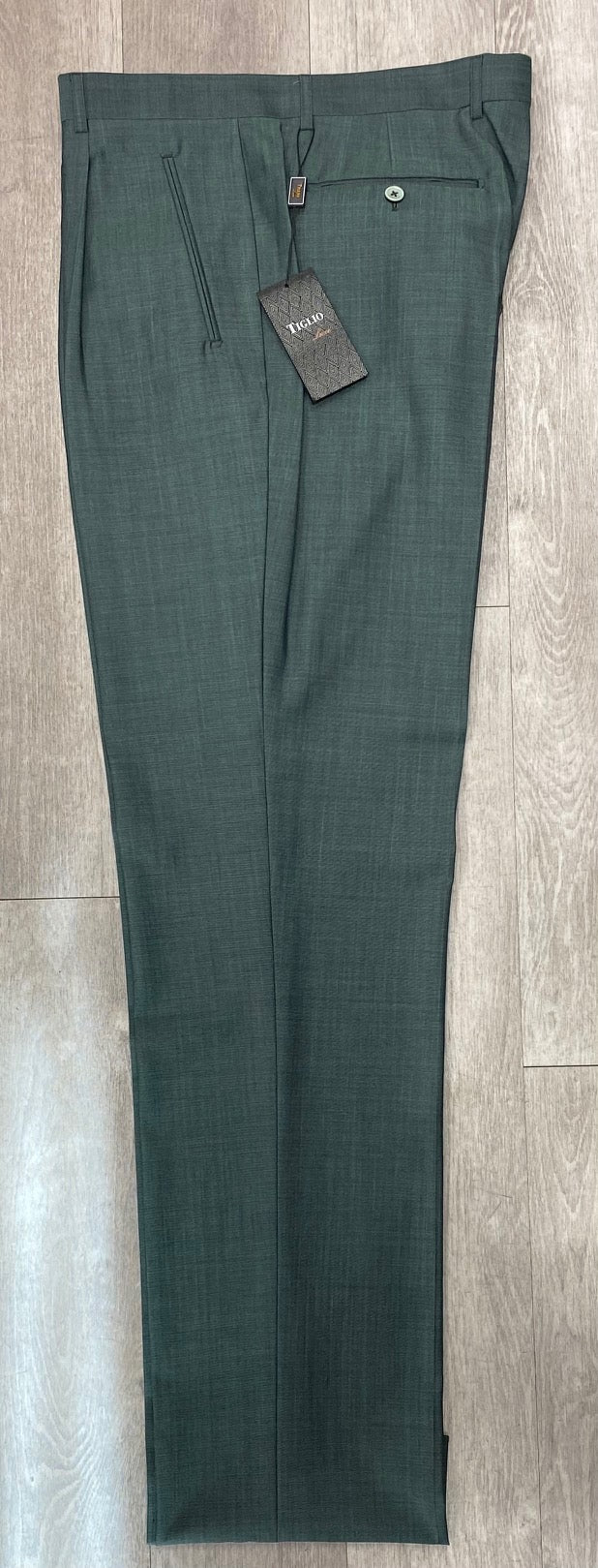 The Tiglio Luxe 2521 Comfort Fit Single Pleated Pants in green, featuring a wide-leg design and crafted from fine wool fabrics, rest elegantly on a wooden floor with a brown tag attached to the waistband.