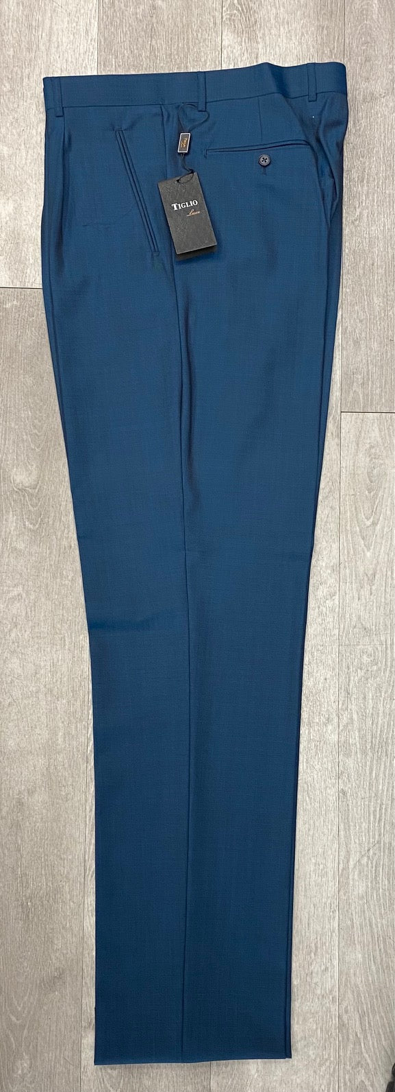 A pair of Tiglio Luxe 2521 Comfort Fit Single Pleated Pants in teal blue, made from extra fine wool and featuring a tag attached, lying flat on a wooden floor.