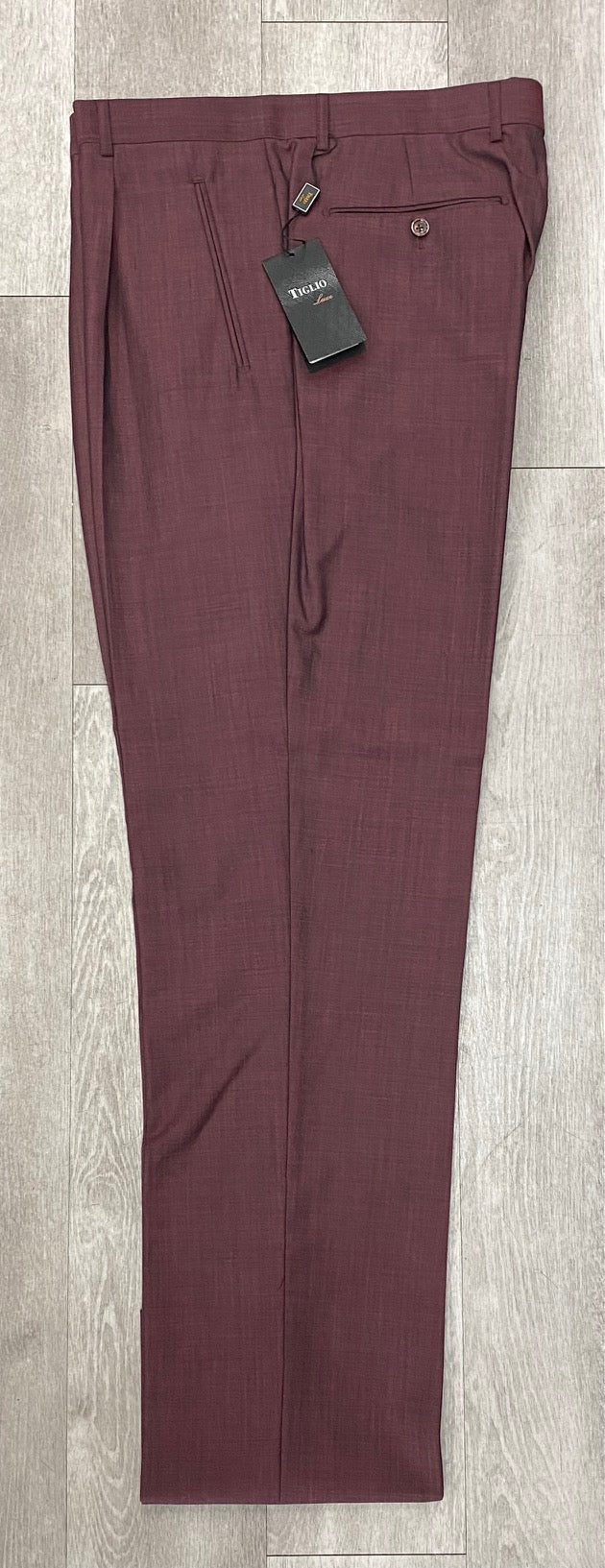 A pair of Tiglio Luxe 2521 Comfort Fit single pleated pants in burgundy, featuring an 18+ inch wide-leg crafted from extra fine wool, with tags attached and elegantly displayed on a wooden floor (SIZE 50 ONLY).