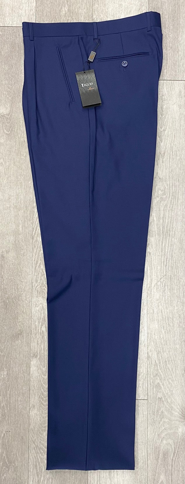 A pair of Tiglio Luxe 2521 Comfort Fit Single Pleated Pants in blue, crafted with an 18+ inch wide-leg and made from extra fine wool. The black brand tag is attached, and the elegant pants are displayed on a light wood floor. (Available in size 50 only.)