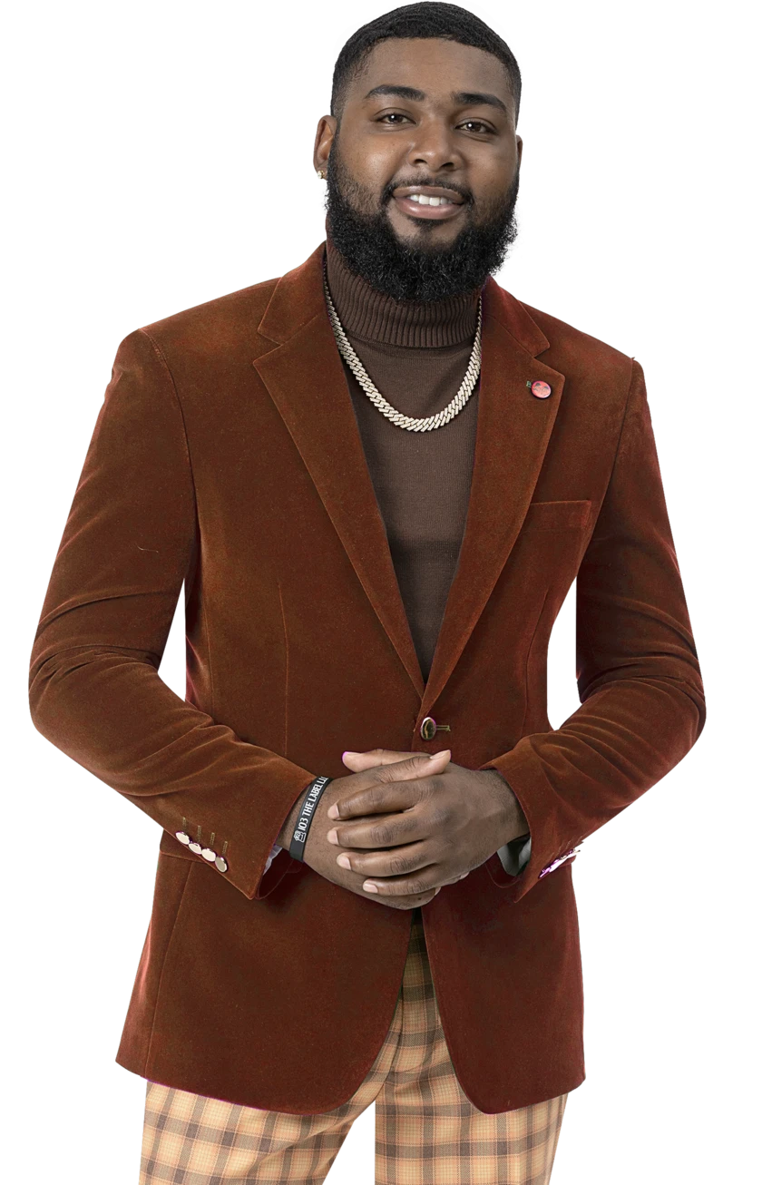 A man with a beard stands against a white background wearing the EJ Samuel Rust Velvet Blazer J134, featuring gold buttons. He pairs it with a brown turtleneck, plaid pants, and jewelry.