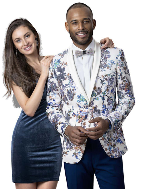 A man and woman pose together. The man wears an EJ Samuel Cream Floral Blazer J99 featuring a modern fit with a floral pattern, complemented by a bow tie, while the woman dazzles in a dark velvet dress adorned with intricate floral and bird sequins.