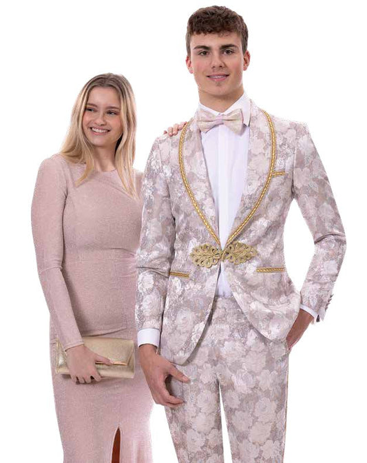 A young woman in a long, light-colored dress stands beside a young man wearing the EJ Samuel Tan Suit JP117 by EJ SAMUEL, complete with a matching floral-patterned bowtie, both smiling at the camera.