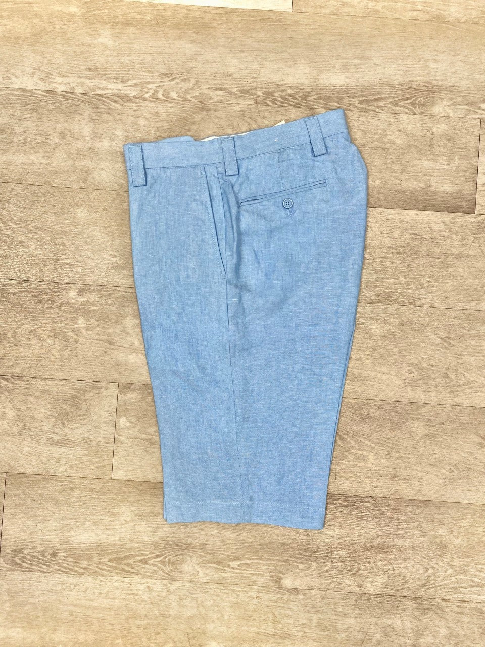 The Inserch Premium Linen Flat Front Shorts in Lake Blue (P21116/P21110) from Inserch are elegantly folded and arranged on a wooden floor, making them an essential addition to any summer wardrobe.