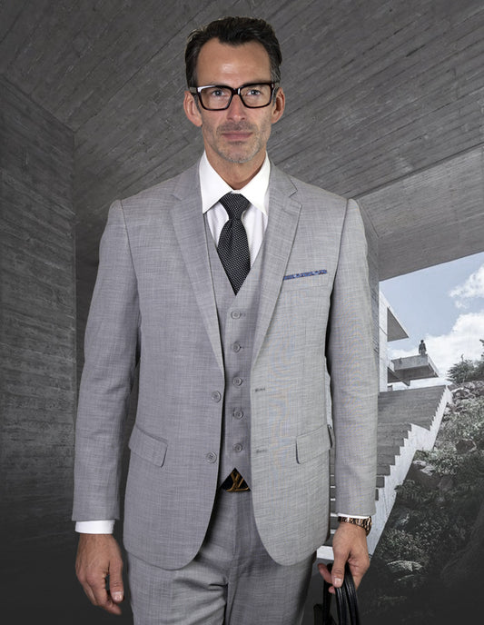 A man wearing the STATEMENT CLOTHING | LAZARO-GREY suit from Statement Clothing stands confidently in front of a concrete structure, holding a bag.