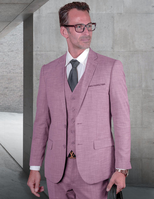 A man wearing the STATEMENT CLOTHING | LAZARO-LAVENDER suit crafted from fine Italian fabric and glasses stands in a concrete hallway, holding a black bag.