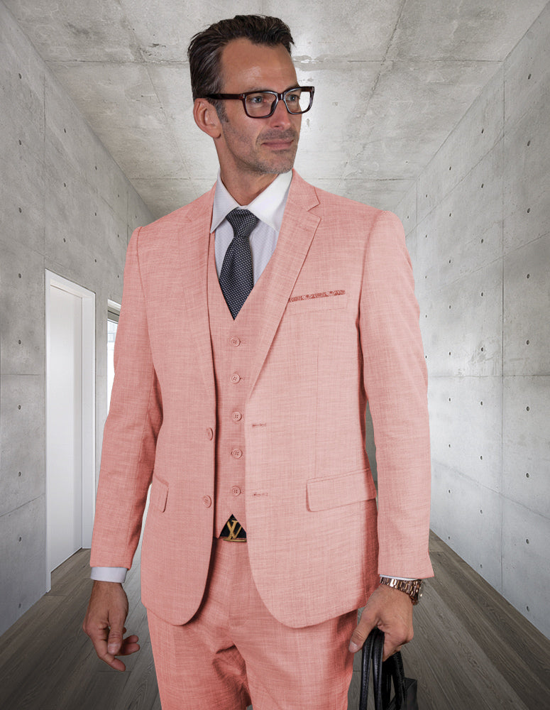 A man in a slim-fit, STATEMENT CLOTHING | LAZARO-PINK suit by Statement Clothing with a white shirt and dark tie stands in a modern, concrete hallway, holding a black bag.