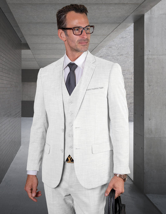 A man in a STATEMENT CLOTHING | LAZARO-WHITE suit, featuring a waistcoat and tie, holds a bag as he stands confidently in a modern concrete hallway.