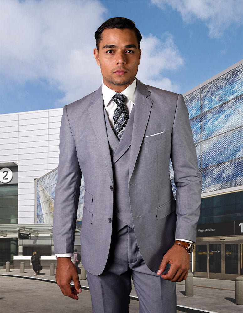 A man in the STATEMENT CLOTHING | LAZIO-GREY tailored fit suit with flat front pants stands confidently in front of a modern building with a blue-patterned facade.