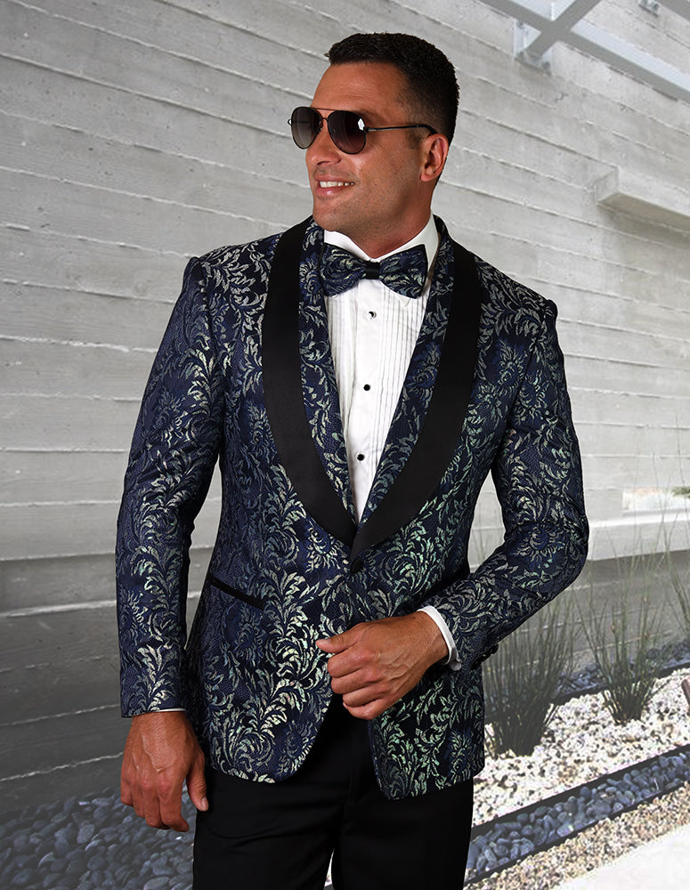 A person wearing the STATEMENT CLOTHING | LJ-100-SAPPHIRE tailored fit suit from Statement Clothing, along with a matching bow tie and stylish sunglasses, stands against a concrete wall backdrop.