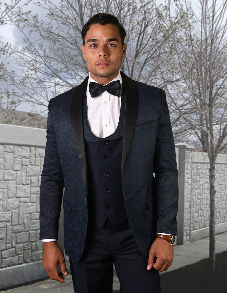 A man wearing the STATEMENT CLOTHING | LOOK-4-NAVY slim fit tuxedo from Statement Clothing, complete with a matching bow tie, stands outdoors framed by a leafless tree and a stone wall.