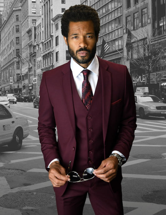 Lorenzo exudes confidence on a bustling city street, dressed in the STATEMENT CLOTHING | LORENZO-BURGUNDY suit by Statement Clothing and holding a pair of sunglasses. The monochrome urban scene, dotted with taxis and skyscrapers, highlights his commanding presence.