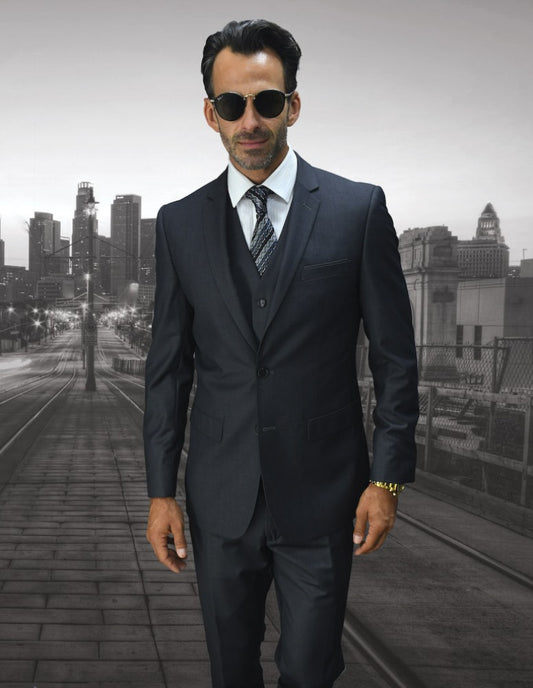 A man in a stylish outfit from Statement Clothing, wearing the LORENZO-CHARCOAL suit with slim fit flat front pants, stands confidently on an urban street with towering skyscrapers in the background.