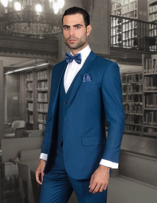 A man wearing the STATEMENT CLOTHING | LORENZO-INDIGO suit from Statement Clothing and a bow tie stands in a library setting.