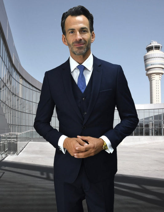 A man in a slim fit STATEMENT CLOTHING | LORENZO-NAVY suit exudes confidence outdoors, with modern architecture and a control tower rising behind him, his flat front pants from Statement Clothing perfectly enhancing the sleek ambiance.