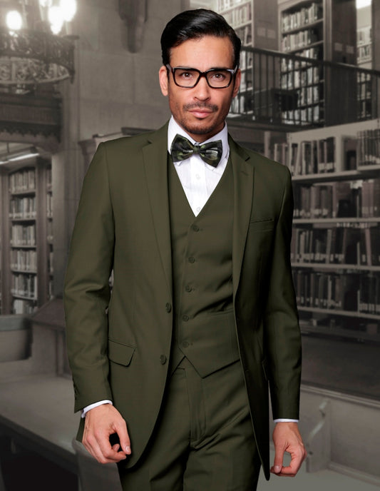 A man wearing the Statement Clothing LORENZO-OLIVE slim fit suit with a bow tie stands in a library, looking forward.