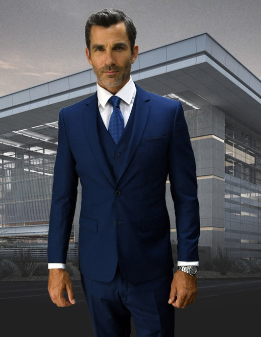 Lorenzo stands confidently before a modern glass building, his poised demeanor accentuated by his well-groomed beard and short dark hair, all while clad in the sleek LORENZO-SAPHIRE slim-fit suit from Statement Clothing.