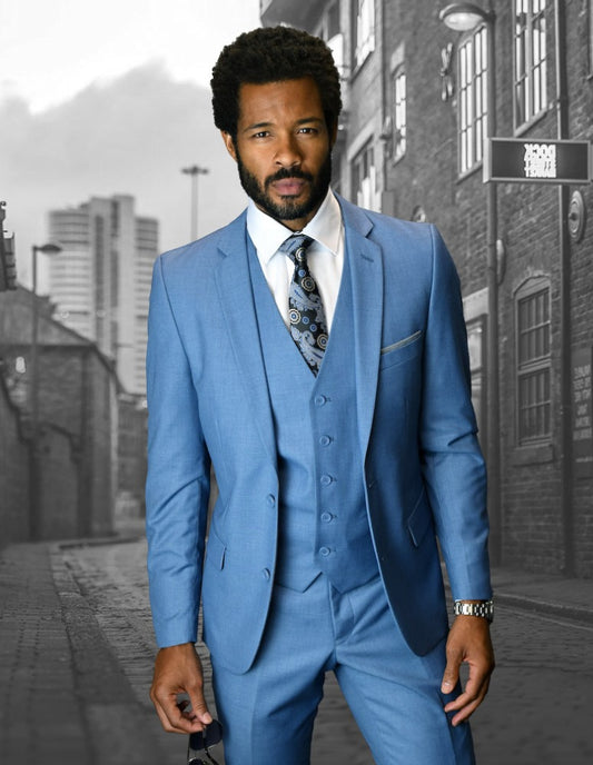 A man in a steel blue, slim fit Lorenzo suit from Statement Clothing stands confidently on an urban street with brick buildings and a cloudy sky in the background.